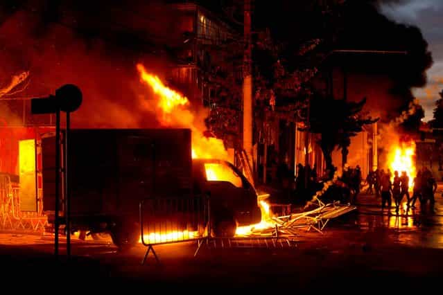 Protesters, right, set cars and stores on fire during a demonstration in Belo Horizonte, Brazil, Wednesday, June 26, 2013. Brazilian anti-government protesters in part angered by the billions spent in World Cup preparations and police clashed Wednesday near the stadium hosting a Confederations Cup football match, with tens of thousands of demonstrators trying to march on the site confronting police firing tear gas and rubber bullets. (Photo by Victor R. Caivano/AP Photo)