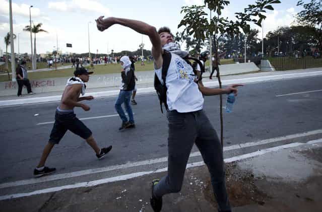 Demonstrators hurl stones to police during clashes between riot police and protesters in Belo Horizonte, Brazil, Wednesday, June 26, 2013. Brazilian anti-government protesters in part angered by the billions spent in World Cup preparations and police clashed Wednesday near the stadium hosting a Confederations Cup football match, with tens of thousands of demonstrators trying to march on the site confronting police firing tear gas and rubber bullets. (Photo by Victor R. Caivano/AP Photo)