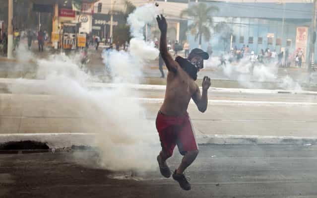 A protester throws a canister of tear gas at police during a demonstration in Belo Horizonte, Brazil, Wednesday, June 26, 2013. Brazilian anti-government protesters in part angered by the billions spent in World Cup preparations and police clashed Wednesday near the stadium hosting a Confederations Cup football match, with tens of thousands of demonstrators trying to march on the site confronting police firing tear gas and rubber bullets. (Photo by Victor R. Caivano/AP Photo)