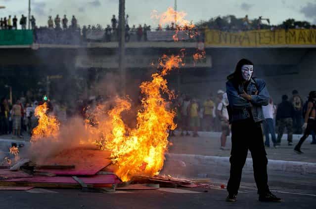 A protester stands by a burning barricade during a demonstration in Belo Horizonte, Brazil, on June 26, 2013. Anti-government protesters, in part angered by the billions spent in World Cup preparations, and police clashed Wednesday near the stadium hosting a Confederations Cup soccer match, with tens of thousands of demonstrators trying to march on the site confronting police firing tear gas and rubber bullets. (Photo by Victor R. Caivano/Associated Press)