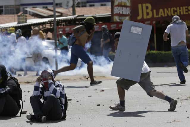 A protester runs with a make-shift shield, right, as others throw rocks at police who are firing tear gas at them a few miles from the soccer stadium where Spain and Italy will play in a Confederations Cup semifinal soccer game in Fortaleza, Brazil, Thursday, June 27, 2013. It's the latest in a series of massive, nationwide protests that have hit Brazil since June 17. Demonstrators are angered about corruption and poor public services despite a heavy tax burden. Protests are also denouncing the billions of dollars spent to host the World Cup and the 2016 Olympics in Rio - money they say should be going toward better hospitals, schools, transportation projects and schools. (Photo by Natacha Pisarenko/AP Photo)