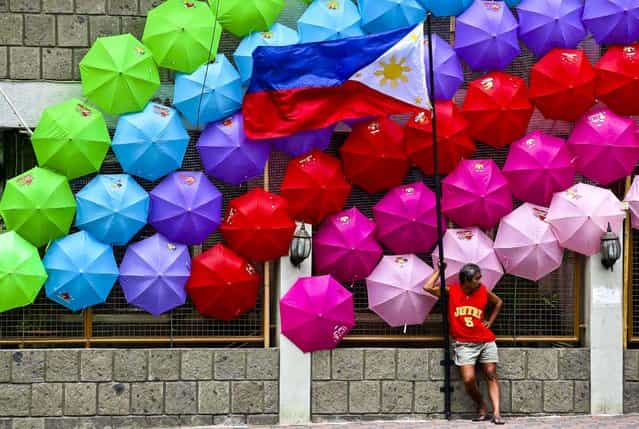 A man stands beside the Philippine flag as colorful umbrellas adorn a village hall in suburban San Juan, east of Manila, Philippines, on June 27, 2013. (Photo by Aaron Favila/Associated Press)