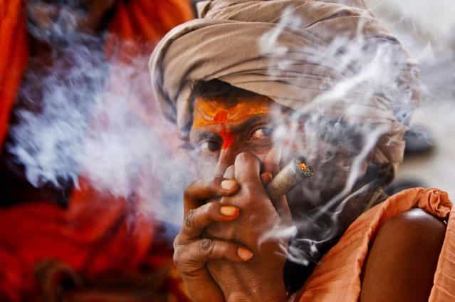 A Hindu holy man smokes as he waits to register for the annual pilgrimage to the Amarnath cave shrine in Jammu, India, on June 28, 2013. Thousands of pilgrims annually visit the remote Himalayan shrine of Amarnath at 12,756 feet above sea level to worship an icy stalagmite representing Shiva, the Hindu god of destruction. (Photo by Channi Anand/Associated Press)