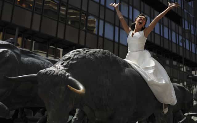 An unnamed actress wearing a wedding dress, gestures on one bull of the Bull Running sculptures, in Pamplona northern Spain on Wednesday, June 26, 2013. The famous festival of San Fermin, begins on July 6, where thousands of people enjoy the famous Pamplona morning bull runs. (Photo by Alvaro Barrientos/AP Photo)