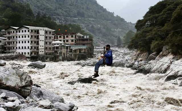 A man crosses over a swollen river with the help of a rope in Govindghat, India, on June 23, 2013. Bad weather hampered efforts Sunday to evacuate thousands of people stranded in the northern India state of Uttarakhand, where at least 1,000 people have died in monsoon flooding and landslides, army officials said. (Photo by Rafiq Maqbool/Associated Press)