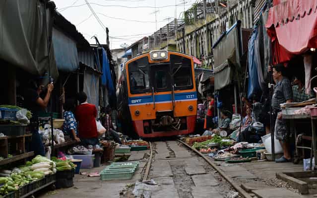 A train passes through a food market in Maeklong, some 60 kilometers south-west of Bangkok, on June 27, 2013. Several times a day, shopkeepers swiftly pack up their food stalls and pull back their canopies to let the trains pass. Once the trains have rumbled through, the crates of vegetables, fish and eggs, are heaved back into their position along the tracks and shoppers return to the tracks they use as a path through the market. (Photo by Christophe Archambault/Getty images)