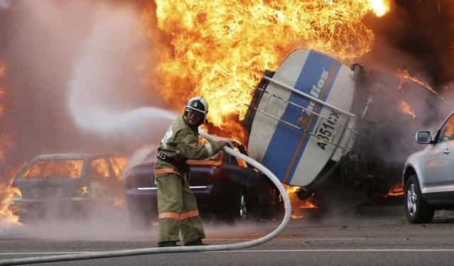 A firefighter tries to extinguish a fire after a road accident in downtown Almaty, on Thursday, June 27, 2013. A multi-story apartment building caught fire in the center of Almaty, Kazakhstan after a road accident, on Thursday, June 27. According to witnesses, the fire is a result of a petrol tank lorry that exploded near Rixos hotel at the crossing killing one person and destroying 20 apartments. (Photo by Sergey Khodanov/AP Photo)
