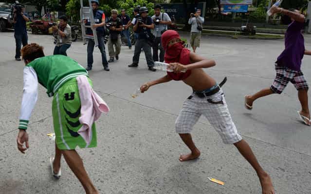 Informal settlers throw bottles at policemen (not pictured) during a clash in Manila on July 1, 2013 after residents blocked a road in anticipation of the demolition of their homes. Philippine informal settlers hurling rocks, improvised explosives and human refuse fought running street battles with riot police on July 1 around a sprawling Manila shantytown that is set for redevelopment. (Photo by Ted Aljibe/AFP Photo)