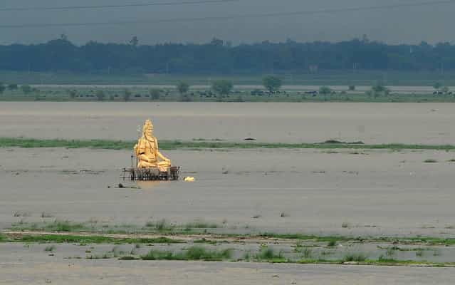 A giant statue of Hindu god Lord Shiva is partially submerged in floodwaters near the Ganges river as the water level of the Ganges and Yamuna rivers rises in Allahabad on July 1, 2013. Construction along river banks will be banned in the devastated north Indian state of Uttarakhand amid concerns unchecked development fuelled June's flash floods and landslides that killed thousands, the state's top official said July 1. (Photo by Sanjay Kanojia/AFP Photo)
