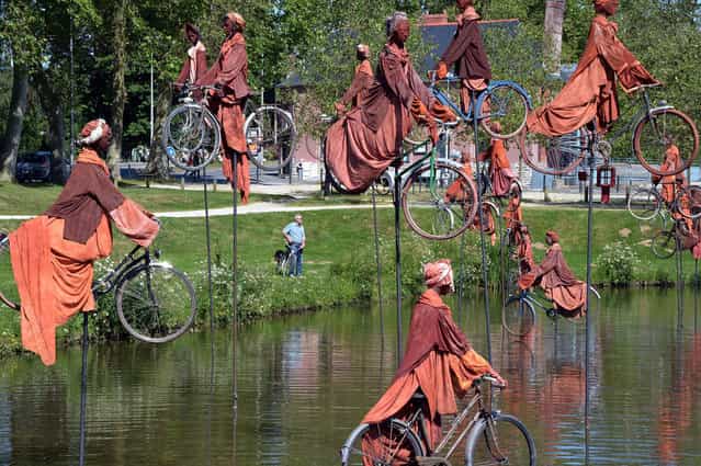 A photo taken on July 1, 2013 shows a sculpture by French artist Guy Lorgeret, entitled [Retour a Betton] ([Return to Betton]), in Betton, a suburb of the western French city of Rennes. The sculpture represents people on bicycles migrating from a bank to another, claiming their freedom, like their refusal to compete. (Photo by Damien Meyer/AFP Photo)