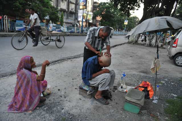 An Indian barber attends to a customer at his roadside stall in Siliguri on July 1, 2013. (Photo by Diptendu Dutta/AFP Photo)