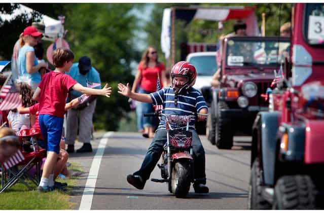 Patrick Ardis, 10, gets a high-five from his friend Porter Rosenberg, 10, left, while riding in the Cordova Independence Day Parade at the Cordova Community Center in Cordova, Tenn., on Thursday, July 4, 2013. (Photo by Jim Weber/AP Photo/The Commercial Appeal)