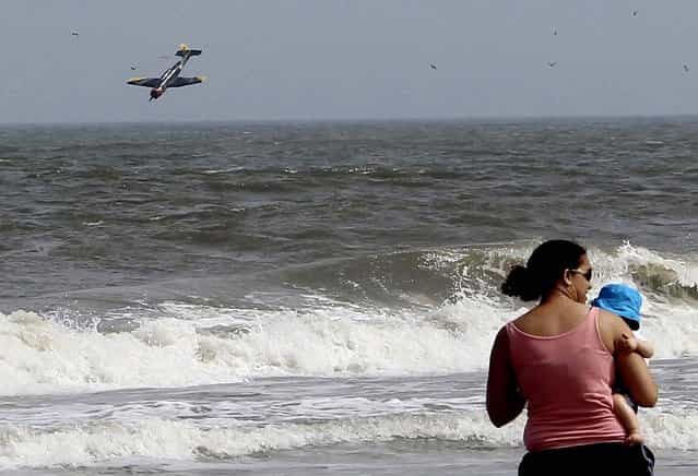 In this photo released on July 1, 2013, a woman holds her child as a plane crashes into the Atlantic Ocean with two off-duty police officers, off Ocean City, Maryland on Sunday. Troopers say the plane took off from the Ocean City Municipal Airport between 3:30 p.m. and 3:45 p.m. Sunday. Maryland State Police identified the men as 27-year-old Joshua D. Adickes of Berlin and 43-year-old Thomas J. Geoghegan Jr. of Ocean City. Both men were officers with the Ocean City Police Department. (Photo by Lisa Rufo/Associated Press)