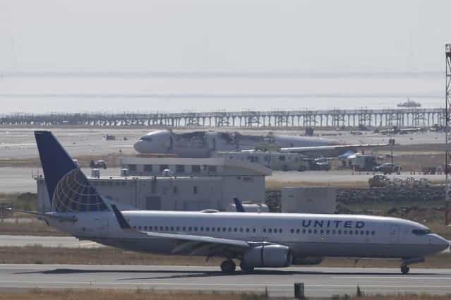 An United Airlines airliner taxis past the wreckage of Asiana Airlines flight 214 at San Francisco International Airport July 7, 2013. Air travel continues to be impacted the day after the Asiana's Boeing 777 from Seoul with 307 people on board crashed and burst into flames, killing two people and sending more than 180 to local hospitals. (Photo by Stephen Lam/Reuters)