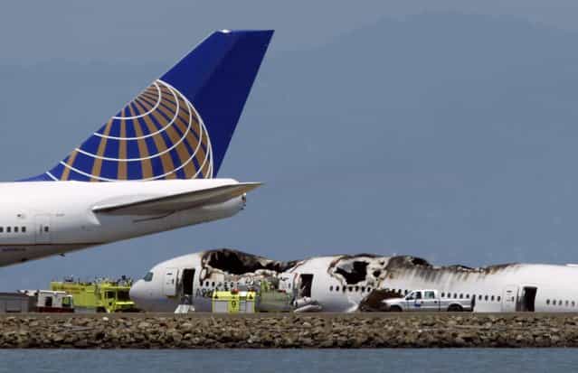 A passenger plane taxis on the runway past an Asiana Airlines Boeing 777 that crashed while landing at San Francisco International Airport in San Francisco, California July 6, 2013. Two people were reported killed and 73 to 103 injured in the crash landing of the Asiana Airlines flight at San Francisco International Airport on Saturday, a city fire department dispatcher said. (Photo by Robert Galbraith/Reuters)
