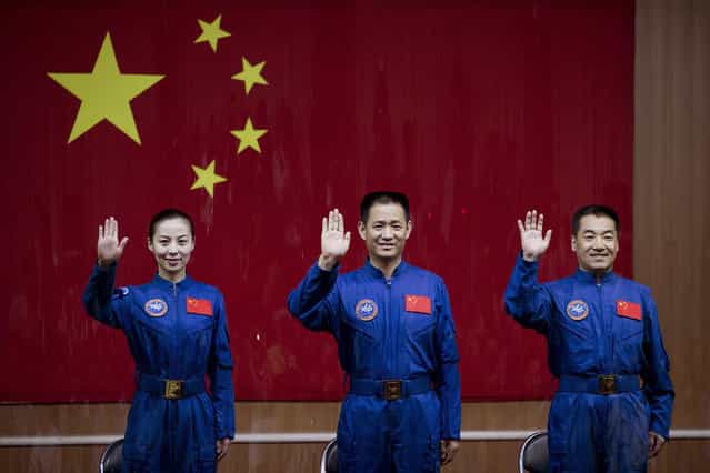 Chinese astronauts from left, Wang Yaping, Nie Haisheng and Zhang Xiaoguang wave from behind a glass enclosure as they arrive to meet the press at the Jiuquan satellite launch center, on June 10, 2013. (Photo by Andy Wong/AP Photo via The Atlantic)