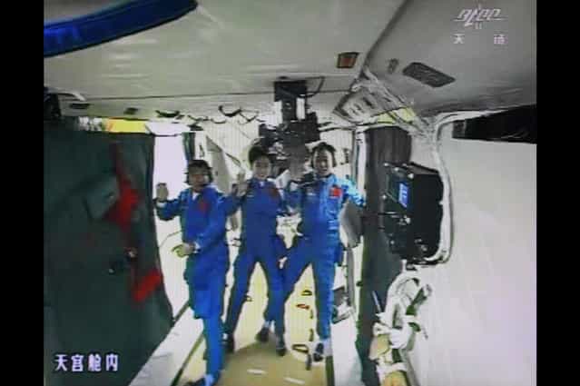 A photo of the giant screen at the Jiuquan space center shows Chinese astronauts (from left) Liu Wang, Jing Haipeng and Liu Yang in the Tiangong-1 module on June 18, 2012. The three astronauts entered an orbiting module for the first time, in a move broadcast live on China's state television. (Photo by STR/AFP Photo via The Atlantic)