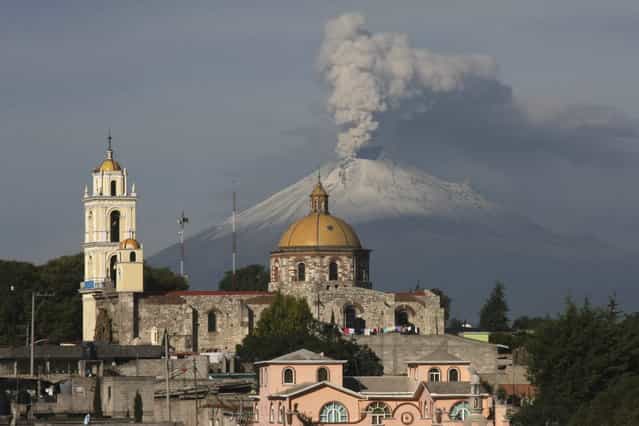 The main church in the town of San Damian Texoloc, Mexico stands in front of the Popocatepetl volcano as is spews ash and vapor early Tuesday, July 9, 2013. Last Saturday, Mexico's National Center for Disaster Prevention raised the volcano alert from Stage 2 Yellow to Stage 3 Yellow, the final step before a Red alert, when possible evacuations could be ordered after the Popocatepetl volcano spit out a cloud of ash and vapor 2 miles (3 kilometers) high over several days of eruptions. (Photo by J. Guadalupe Perez/AP Photo)