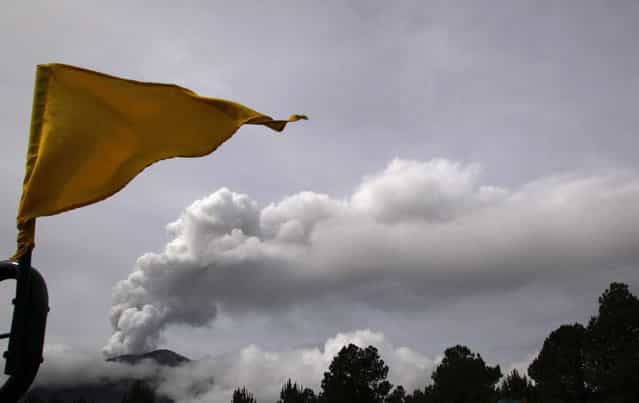 A Stage 3 Yellow flag flies in the Paso de Cortes area near Popocatepetl volcano, behind left, in Mexico, Monday, July 8, 2013. Mexico's National Center for Disaster Prevention raised the volcano alert to Stage 3 Yellow, the final step before a Red alert, when possible evacuations could be ordered. A Stage 3 Yellow alert had been in effect during eruptions earlier this year until early June, when it was lowered. (Photo by Marco Ugarte/AP Photo)