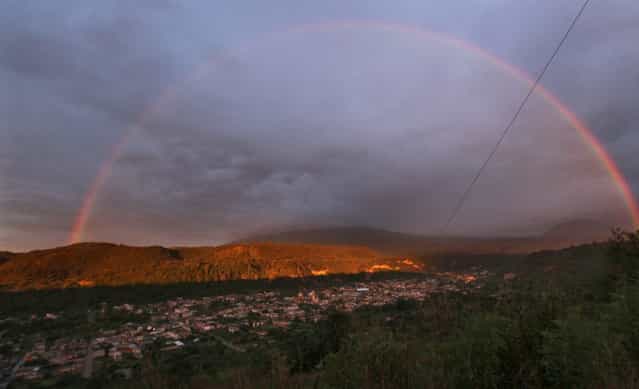 A rainbow forms over the town of Santiago Xalizintla where the Popocatepetl volcano, behind center, is covered by clouds in Mexico, Monday, July 8, 2013. The Environment Ministry has urged residents to take preventive measures to deal with the ash, including wearing dust masks, covering water supplies and staying indoors as needed. (Photo by Marco Ugarte/AP Photo)