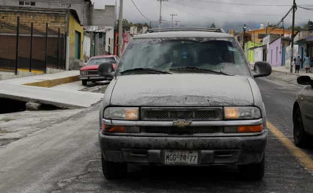 Volcanic ash coats the streets and a vehicle in San Pedro Nexapa, Mexico, Saturday, July 6, 2013. Just east of Mexico City, the Popocatepetl volcano has spit out a cloud of ash and vapor 2 miles (3 kilometers) high over several days of eruptions. Mexico's National Center for Disaster Prevention raised the volcano alert from Stage 2 Yellow to Stage 3 Yellow, the final step before a Red alert, when possible evacuations could be ordered. (Photo by Arturo Andrade/AP Photo)
