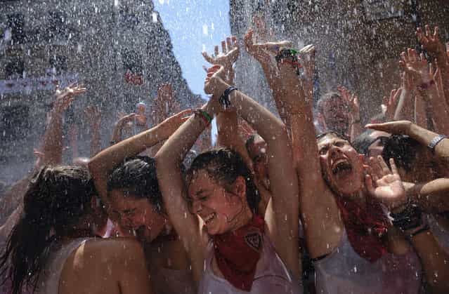 Revelers enjoy being sprayed with water from a balcony in Ayuntamiento square, in Pamplona, northern Spain on Saturday, July 6, 2013, as they celebrate the start of Spain's most famous bull-running festival with the annual launch of the [chupinazo] rocket. (Photo by Alvaro Barrientos/AP Photo)