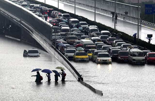 This picture taken on July 7, 2013 shows people walking through a flooded street in Wuhan, central China's Hubei province after a heavy storm. A strong storm hit Wuhan on July 6 and July 7, paralysing transport in multiple places, local media reported. (Photo by AFP Photo)
