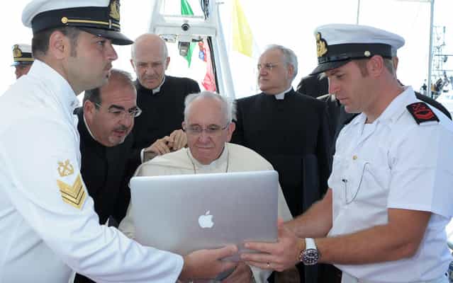 This handout picture released by the Vatican press office on July 8, 2013 shows Pope Francis looking at a computer while receiving explanations on a boat off Lampedusa island, a key destination of tens of thousands of would-be immigrants from Africa, during his visit on July 8, 2013. In a visit stripped of the usual pomp of papal travel, Francis will cast a wreath into the sea and hold a mass of mourning with a simple cross made from the wood of rickety fishing boats that migrants arrive on. (Photo by Osservatore Romano/AFP Photo)