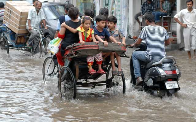 Indian commuters make their way through a waterlogged street after heavy monsoon rains fell in Jalandhar, on July 9, 2013. Authorities have raised to 5,500 the estimated number of people who perished in devastating floods that swept the northern Indian state of Uttarakhand last month. (Photo by Shammi Mehra/Getty Images)