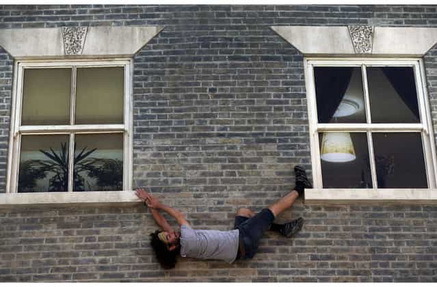 A visitor enjoys an art installation by Argentine artist Leandro Erlich in east London, Tuesday, July 9, 2013. Internationally known for his three-dimensional visual illusions, Erlich has been commissioned to create a new installation in Dalston area of the capital. Resembling a theatre set, the detailed facade of a Victorian terraced house, recalling those that once stood on the street, lies horizontally on the ground with mirrors positioned overhead. The reflections of visitors give the impression they are standing on, suspended from, or scaling the building. (Photo by Lefteris Pitarakis/AP Photo)