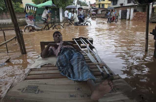 A physically disabled man rests as commuters on rickshaw cross a waterlogged street in Gauhati, India, Tuesday, July 16, 2013. (Photo by Anupam Nath/AP Photo)