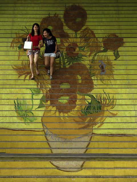 Shoppers walk down stairs featuring a five-metre-high reproduction of Vincent van Gogh's signature painting [Sunflowers], at the entrance to Ocean Terminal in Hong Kong July 15, 2013. A premium three-dimensional reproduction of works of Van Gogh, the RELIEVO collection, approved by the curators of the Van Gogh Museum in Amsterdam, is on display at a gallery inside Harbour City shopping mall attached to the terminal. (Photo by Bobby Yip/Reuters)