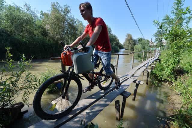 A man rides his bikeon the wooden pedestrian way in the small city of Vylkove, Odessa region, on July 11, 2013. Vylkove is also known as [The Ukrainian Venice] thanks to a number of canals inside its territory – the reason why boating is a more common method of transport than an automobile. The city is the last settlement on bank of the Danube before the Black Sea. The Danube river is Europe's second longest river after the Volga. From Black forest of Germany to the Black Sea it passes through or touches the borders of ten countries of Central Europe. (Photo by Sergei Supinsky/AFP Photo)
