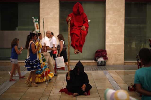 Women wearing traditional Sevillana dresses (L) walk past street performers at Marques de Larios street in downtown Malaga, southern Spain, July 18, 2013. (Photo by Jon Nazca/Reuters)