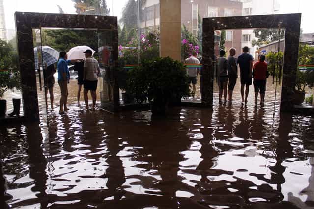 Citizens look on as water flooded streets in a lobby on July 19, 2013 as heavy storm hit Kunming, southwest China's Yunnan province. At least 295 people have been confirmed dead or missing after rainstorms and Typhoon Soulik hit China, causing floods, landslides and buildings to collapse, the government said on July 15. (Photo by AFP Photo)