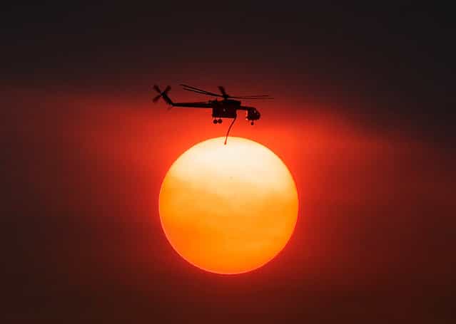 Smoke from the Mountain Fire obscures the sun as a fire fighting helicopter heads to fight the Mountain Fire after picking up water from Lake Hemet July 18, 2013 near Idyllwild, California. The massive wildfire in Riverside County has grown to 23,000 acres and is advancing towards the mountain town of Idyllwild on one front and city of Palm Springs on the other front destroying several homes and forcing the evacuation of 6,000 people. (Photo by Kevork Djansezian/Getty Images)