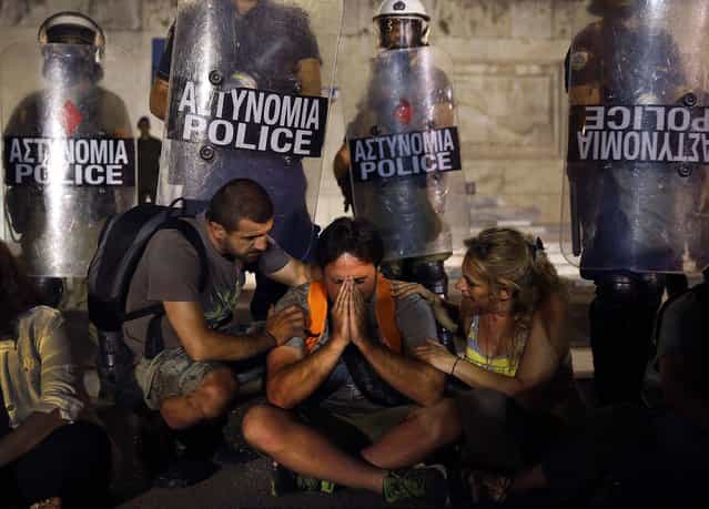 Municipal public school guard Yiorgos Avramidis, 43, married with two children of three and six, from the northern Greek town of Edessa, is comforted by colleagues in front of a police line guarding the Greek parliament in Athens, as Greece's shaky coalition government scraped through a vote on a bill to sack public sector workers, on July 17, 2013. The bill includes deeply divisive plans for a transfer and layoff scheme for 25,000 public workers - mainly teachers and municipal police - that had triggered a week of almost daily marches, rallies and strikes in protest. Avramidis is one of the more than 2,000 public school guards who lost their jobs. (Photo by Yannis Behrakis/Reuters)