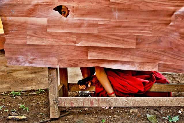A novice Tibetan Buddhist monk peeps through a hole as he hides behind a desk holding a toy gun during a break from their spiritual leader the Dalai Lama's religious sermon outside the Gyudmed Tantric Monastery southwest of Bangalore, India, on July 15, 2013. (Photo by Aijaz Rahi/Associated Press)