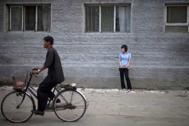 In this Friday, June 21, 2013 photo, a woman stands on a street as a man cycles past in Haeju city, in South Hwanghae Province, North Korea. (Photo by Alexander F. Yuan/AP Photo)