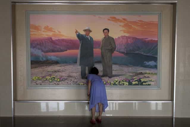In this Friday, June 21, 2013 photo, a woman arranges flowers in front of a painting depicting the late leaders Kim Il Sung, left, and Kim Jong Il at the lobby of a hotel in Haeju city, South Hwanghae Province, North Korea. (Photo by Alexander F. Yuan/AP Photo)
