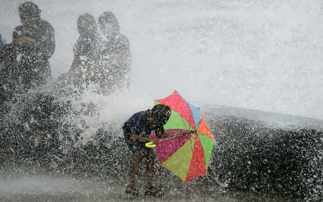 An Indian boy holds an umbrella as waves break over a seawall while monsoon rain falls, on July 25, 2013. The monsoon season, which runs from June to September, accounts for about 80% of India's annual rainfall, vital for a farm economy which lacks adequate irrigation facilities. (Photo by Punit Paranjpe/AFP Photo)