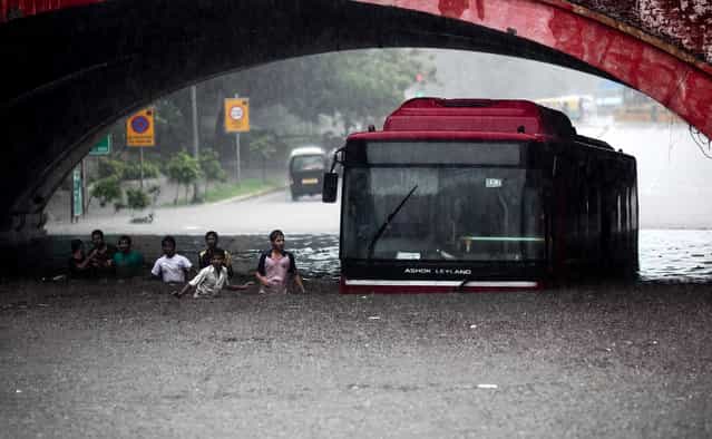 Indians wade past a bus submerged in rainwater in New Delhi, India, Saturday, July 20, 2013. Heavy rainfall lashed the national capital Saturday, flooding streets and homes and choking the city with traffic jams. (Photo by AP Photo)