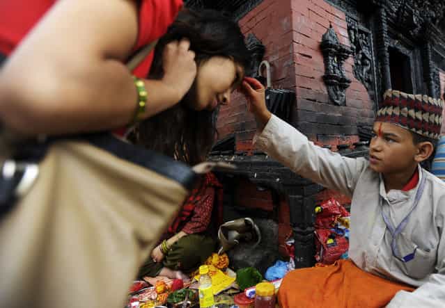 A young Nepalese Hindu priest offers tika blessings to Hindu devotees at The Pashupatinath Temple in Kathmandu on July 22, 2013. According to the Nepali calendar, Shravan is considered the holiest month of the year with each Monday of the month known as Shravan Somvar when worshippers offer prayers for a happy and prosperous life. (Photo by Prakash Mathema/AFP Photo)