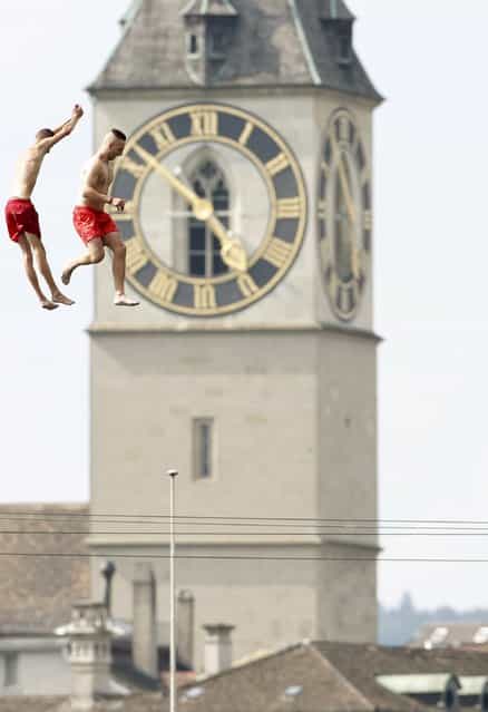 Two men jump from a 10 metre (32ft) high public diving platform into Lake Zurich during a sunny summer day in Zurich July 25, 2013. In the background is seen St. Peter church. (Photo by Arnd Wiegmann/Reuters)