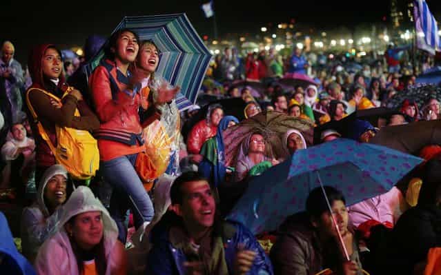 People watch a video screen as Pope Francis celebrates Mass on Copacabana Beach in Rio de Janeiro, on July 25, 2013. (Photo by Mario Tama/Getty Images)