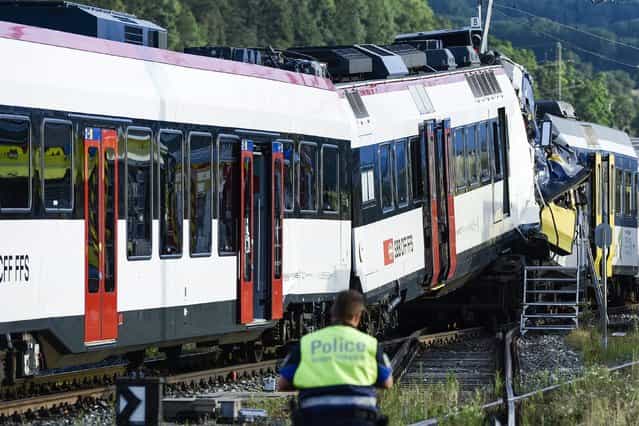 A police officer inspects the site where two passenger trains collided head-on in Granges-pres-Marnand, western Switzerland, Monday, July 29, 2013. Numerous people have been injured. (Photo by Laurent Gillieron/AP Photo/Keystone)