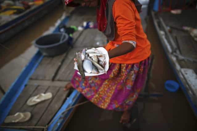 An ethnic Cham Muslim woman carries a plate with fish prepared for iftar (breaking fast) on the banks of Mekong river in Phnom Penh July 27, 2013. About 100 ethnic Cham families, made up of nomads and fishermen without houses or land who arrived at the Cambodian capital in search of better lives, live on their small boats on a peninsula where the Mekong and Tonle Sap rivers meet, just opposite the city's centre. The community has been forced to move several times from their locations in Phnom Penh as the land becomes more valuable. They fear that their current home, just behind a new luxurious hotel under construction at the Chroy Changva district is only temporary and that they would have to move again soon. (Photo by Damir Sagolj/Reuters)