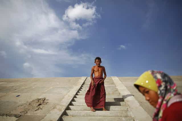 An ethnic Cham Muslim man walks on a flight of steps at the banks of Tonle Sap river in Phnom Penh July 27, 2013. About 100 ethnic Cham families, made up of nomads and fishermen without houses or land who arrived at the Cambodian capital in search of better lives, live on their small boats on a peninsula where the Mekong and Tonle Sap rivers meet, just opposite the city's centre. The community has been forced to move several times from their locations in Phnom Penh as the land becomes more valuable. They fear that their current home, just behind a new luxurious hotel under construction at the Chroy Changva district is only temporary and that they would have to move again soon. (Photo by Damir Sagolj/Reuters)