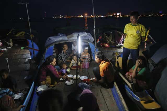 Ethnic Cham Muslim people eat their iftar (breaking fast) meals on the banks of Tonle Sap river in Phnom Penh July 29, 2013. About 100 ethnic Cham families, made up of nomads and fishermen without houses or land who arrived at the Cambodian capital in search of better lives, live on their small boats on a peninsula where the Mekong and Tonle Sap rivers meet, just opposite the city's centre. The community has been forced to move several times from their locations in Phnom Penh as the land becomes more valuable. They fear that their current home, just behind a new luxurious hotel under construction at the Chroy Changva district is only temporary and that they would have to move again soon. (Photo by Damir Sagolj/Reuters)