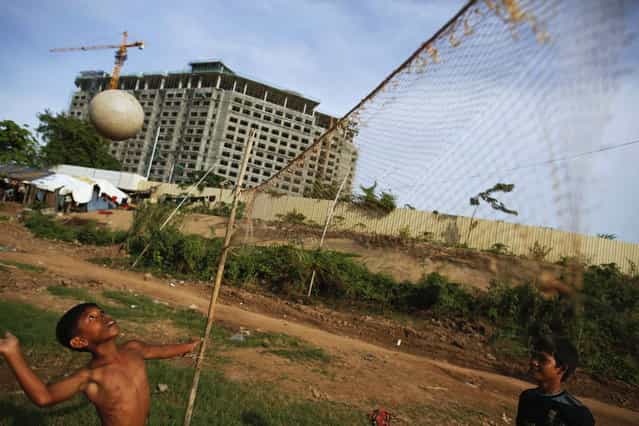 Ethnic Cham Muslim children play volleyball in front of a hotel under construction on the banks of Mekong river in Phnom Penh July 30, 2013. About 100 ethnic Cham families, made up of nomads and fishermen without houses or land who arrived at the Cambodian capital in search of better lives, live on their small boats on a peninsula where the Mekong and Tonle Sap rivers meet, just opposite the city's centre. The community has been forced to move several times from their locations in Phnom Penh as the land becomes more valuable. They fear that their current home, just behind a new luxurious hotel under construction at the Chroy Changva district is only temporary and that they would have to move again soon. (Photo by Damir Sagolj/Reuters)
